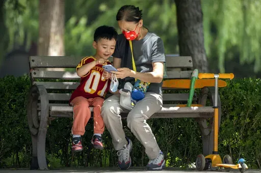 A woman wearing a face mask and a child look at a cellphone as they sit on a bench at a public park in Beijing, on June 2, 2022. As the week-long Lunar New Year holidays in China draw near with promises of feasts and red envelopes stuffed with cash, children have yet another thing to look forward to - one extra hour of online games each day. (AP Photo/Mark Schiefelbein, File)