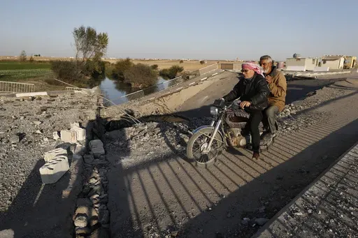 Syrian citizens ride a motorcycle as they cross a bridge that links to Lebanon which was destroyed on Oct. 24 by an Israeli airstrike, in Qusair, Syria, Sunday, Oct. 27, 2024. (AP Photo/Omar Sanadiki)