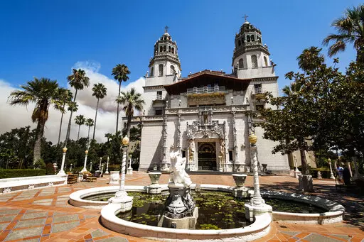 Smoke from a wildfire billows from a ridge line behind famed facade of Hearst Castle in San Simeon, Calif., on Aug. 20, 2016. California's famous Hearst Castle will reopen to the public in May, 2022, after a two-year closure due to the pandemic and severe rainstorm damage that prompted a $13.7 million renovation. (Joe Johnston/The Tribune of San Luis Obispo via AP, File)