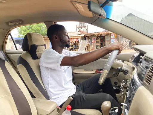 Adenekan Ayomide, 27, an undergraduate student turned a taxi driver following nationwide university strike, poses for a photograph inside his taxi in Abuja, Nigeria, Tuesday, May 10, 2022. “Nobody is talking about school again,” said Ayomide, who said he is now working more than one job and the budget he had for getting through university now looks unrealistic. (AP Photo/Chinedu Asadu)