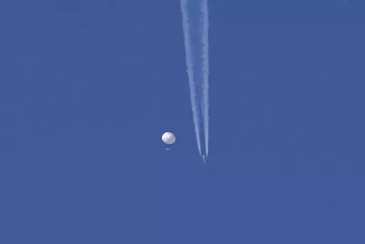 In this photo provided by Brian Branch, a large balloon drifts above the Kingstown, N.C. area, with an airplane and its contrail seen below it. The United States says it is a Chinese spy balloon moving east over America at an altitude of about 60,000 feet (18,600 meters), but China insists the balloon is just an errant civilian airshipused mainly for meteorological research that went off course due to winds and has only limited “self-steering” capabilities. (Brian Branch via AP)