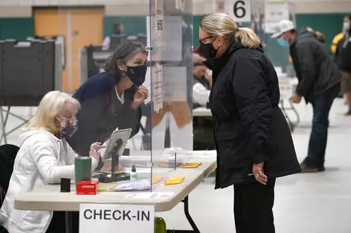 A poll worker, center left, speaks through a plastic barrier while assisting a voter in a polling station at Marshfield High School, Nov. 3, 2020, in Marshfield, Mass. A bipartisan effort among states to combat voter fraud has found itself in the crosshairs of conspiracy theories fueled by Donald Trump’s false claims about the 2020 presidential election and now faces an uncertain future. (AP Photo/Steven Senne, File)
