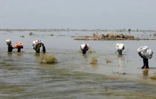 Victims of heavy flooding from monsoon rains crowd carry relief aid through flood water in the Qambar Shahdadkot district of Sindh Province, Pakistan, Sept. 9, 2022. The United Nations says weather disasters costing $200 million a day and irreversible climate catastrophe looming show the world is “heading in the wrong direction.” (AP Photo/Fareed Khan, File)