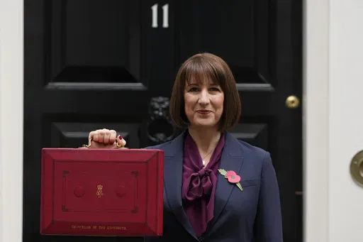 Britain's Chancellor of the Exchequer, Rachel Reeves, holds up the traditional red ministerial box containing her budget speech, as she poses for the media outside No 11 Downing Street, before departing to the House of Commons to deliver the budget in London, Wednesday, Oct. 30, 2024. (AP Photo/Kirsty Wigglesworth)