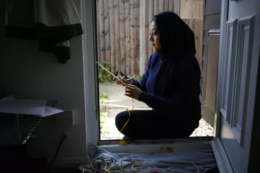Bilqis Alam, an energy advisor from the South East London Community Energy co-operative (Selce), installs draught proofing rubber strips to the front door frame of the home of her client Tia Rutherford, in south east London, Tuesday, March 22, 2022. People across the United Kingdom will face tough choices in coming months as energy costs for millions of households are set to rise by 54% on Friday. It's the second big jump in energy bills since October, and a third may be ahead as rebounding dema