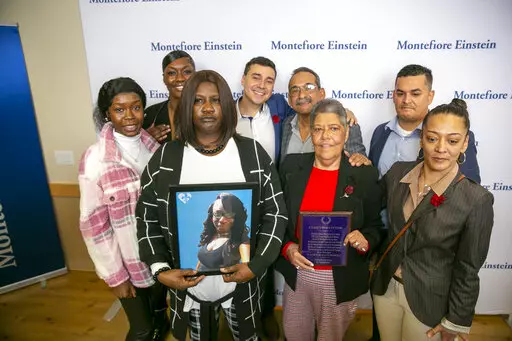 Bridgette Newton holds a picture of her late daughter Brittany Newton next to Miriam Nieves, holding a plaque, who received Brittany Newton's heart in a transplant at Montefiore Moses Hospital in the Bronx borough of New York, on Tuesday, Nov. 22, 2022.Their families stand with them. Doctors at the hospital say the transplant, performed in April, is the first time a heart from an HIV-positive donor was successfully transplanted into an HIV-positive recipient. (AP Photo/Ted Shaffrey)