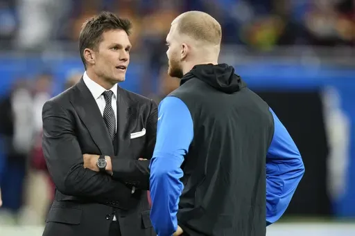 Tom Brady, left, talks with Detroit Lions defensive end Aidan Hutchinson before an NFL football divisional playoff game against the Washington Commanders, Saturday, Jan. 18, 2025, in Detroit. (AP Photo/Seth Wenig)