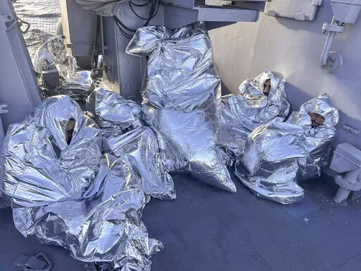 In this photo provided by the Greek Coast Guard, some of the nine men who survived a shipwreck and were found on an uninhabited islet are covered with a thermal blankets as they sit aboard a Greek Coast guard vessel, in the Aegean Sea, Greece, on Tuesday, Nov. 1, 2022. A major search and rescue operation was underway Tuesday for dozens of people missing after the boat they were on capsized and sank in stormy weather overnight off the coast of an island near the Greek capital. The coast guard sai