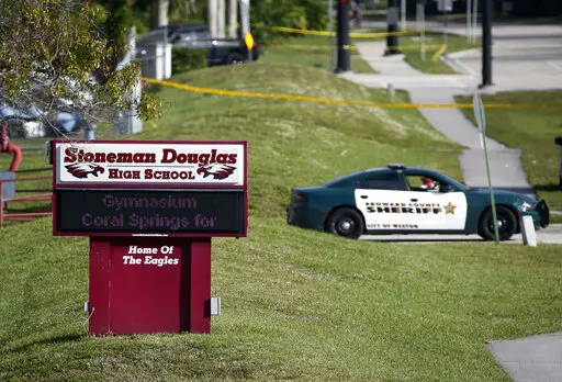FILE- Law enforcement officers block off the entrance to Marjory Stoneman Douglas High School  Feb. 15, 2018 in Parkland, Fla., following a deadly shooting at the school. The families of most of those killed in the 2018 Florida high school massacre have settled their lawsuit against the federal government. Sixteen of the 17 killed at Marjory Stoneman Douglas High in Parkland had sued over the FBI’s failure to stop the gunman even though it had received information he intended to attack. The se
