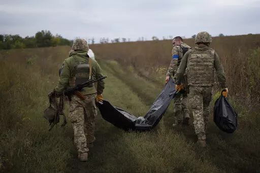 Ukrainian servicemen carry a bag containing the body of a Ukrainian soldier, center, as one of them, right, carries the remains of a body of a Russian soldier in a retaken area near the border with Russia in Kharkiv region, Ukraine, Saturday, Sept. 17, 2022. (AP Photo/Leo Correa)