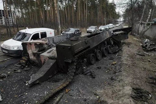 Cars drive past a destroyed Russian tank as a convoy of vehicles evacuating civilians leaves Irpin, on the outskirts of Kyiv, Ukraine, March 9, 2022. Thousands of patients in Ukraine are receiving lifesaving medicines to treat HIV and opioid addiction through a U.S.-funded group still operating despite the Russian invasion. Supplies are running short and making deliveries is a complicated calculus with unpredictable risks. (AP Photo/Vadim Ghirda, File)