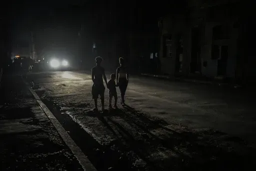 Residents are illuminated by the headlights of a car during a blackout after a major power plant failed in Havana, Cuba, Oct. 18, 2024. (AP Photo/Ramon Espinosa, File)