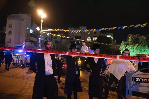 Ultra-Orthodox Jews stand behind police tape after a stabbing attack in the town of Elad, Israel, Thursday, May 5, 2022. Israeli medics say at least three people were killed in a stabbing attack near Tel Aviv on Thursday night. Israeli police said they suspect it was a militant attack. (AP Photo/Maya Alleruzzo)