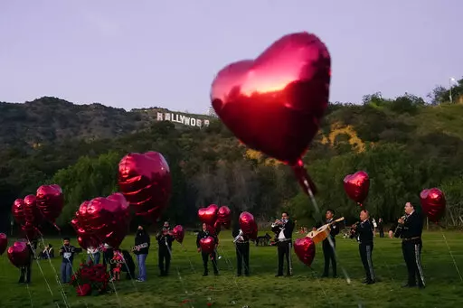 A Mexican Mariachi band surrounded by heart-shaped balloons awaits the arrival of a couple's wedding proposal ceremony at the Lake Hollywood Park in Los Angeles, on Valentine's Day, Monday, Feb. 14, 2022. Attending weddings can be expensive, between travel and lodging, gifts and extra events like bachelor and bachelorette parties. So plan ahead for these expenses, particularly as wedding season approaches and celebrations that were postponed or rescheduled reappear on your calendar.   (AP Photo/