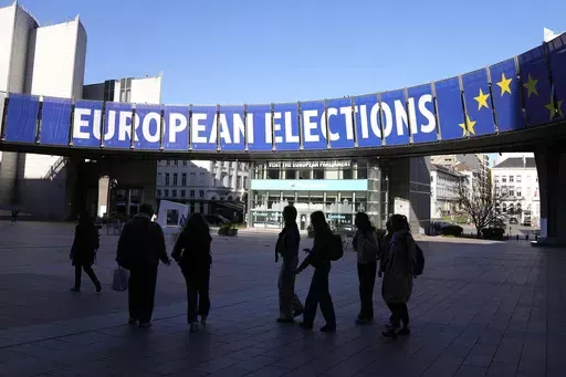 A group stands under an election banner outside the European Parliament in Brussels on April 29, 2024. In an increasingly vitriolic political climate, the last thing needed in the runup to the June European Union elections was an assassination attempt on one of the bloc’s most controversial figures. (AP Photo/Virginia Mayo, File)