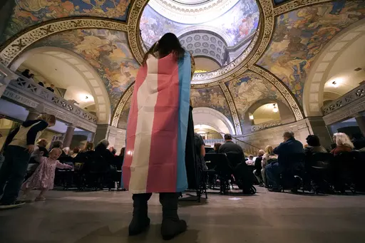 Glenda Starke wears a transgender flag as a counter protest during a rally in favor of a ban on gender-affirming health care legislation, March 20, 2023, at the Missouri Statehouse in Jefferson City, Mo. A Missouri judge said Friday, Aug. 25, that a law banning gender-affirming treatments for minors can take effect. St. Louis Circuit Judge Steven Ohmer ruled that the law will kick in Monday, Aug. 28, as previously scheduled. (AP Photo/Charlie Riedel, File)