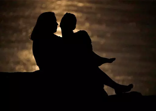 In this June 27, 2018, file photo a couple is silhouetted against moonlight reflecting off the Missouri River as they watch the full moon rise beyond downtown buildings in Kansas City, Mo. While money can be a source of stress in relationships, it can also spark romance if you use money dates to focus on your goals as a couple. First, consider your own goals and ask your partner about their values. Next, identify common goals, such as teaming up to vanquish debt or planning a vacation. Then sche