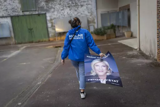 Emma Mino holds an electoral poster of French far-right presidential candidate Marine Le Pen, Tuesday, March 29, 2022 in Le Temple-De-Bretagne, western France. Marine Le Pen’s vision for France if the far-right leader wins Sunday’s runoff presidential election would include a ban on Muslim headscarves in public, schoolchildren in uniforms and laws passed by referendum.  (AP Photo/Jeremias Gonzalez, File)