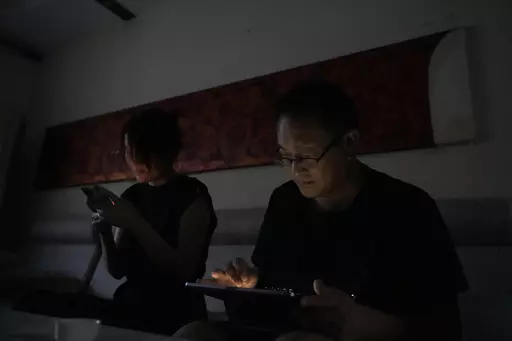 Wang Quanzhang and his wife Li Wenzu look at their phone and laptop in the dark after power was cut off for their apartment in Beijing's Changping district, Tuesday, June 20, 2023. Disbarred human rights lawyer Wang Quanzhang has been forced to move 13 times in two months as part of a pattern of harassment against him and three other prominent rights advocates in Beijing that is further squeezing the country's battered civil rights community. (AP Photo/Ng Han Guan)