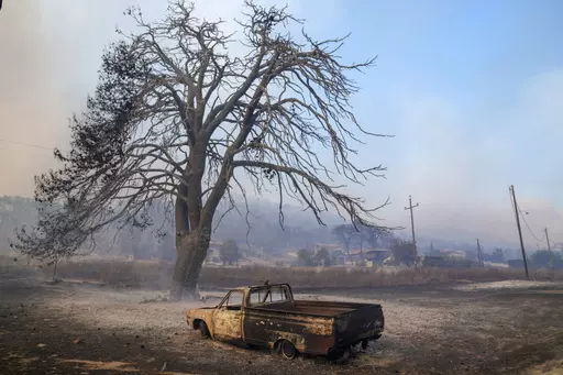 A damaged car stands in front of a burned tree near Loutraki 80 Kilometres west of Athens, Greece, Monday, July 17, 2023. Two wildfires threatened homes in areas outside Athens, where strong winds made the flames difficult to contain. Most of southern Greece, including greater Athens, was an elevated level of alert for fire risk, while more extreme temperatures are expected later this week. (AP Photo/Petros Giannakouris)