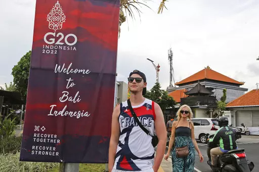 Tourists walk past a G20 banner in Nusa Dua, Bali, Indonesia on Friday, Nov. 11, 2022. The dozens of world leaders and other dignitaries traveling to Bali for the G-20 summit will be drawing a welcome spotlight on the revival of the tropical island's ailing tourism sector after a two-year closure to foreign travelers due to the pandemic. (AP Photo/Firdia Lisnawati)