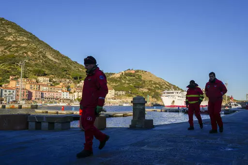 Firefighters walk on a pier of the port of the tiny Tuscan island of Isola del Giglio, Italy, as a ferry boat enters it, Thursday, Jan. 13, 2022. Italy on Thursday is marking the 10th anniversary of the Costa Concordia cruise ship disaster with a daylong commemoration, honoring the 32 people who died but also the extraordinary response by the residents of Giglio who took in the 4,200 passengers and crew from the ship on that rainy Friday night and then lived with the Concordia carcass for anothe