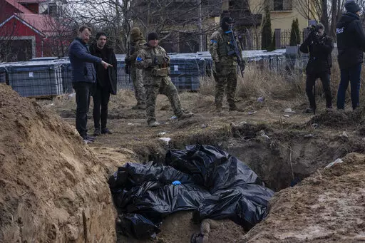 People stand next to a mass grave in Bucha, on the outskirts of Kyiv, Ukraine, April 4, 2022. AP journalists saw dozens of bodies in Bucha, many of them shot at close range, and some with their hands tied behind them. (AP Photo/Rodrigo Abd, File)