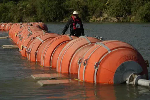 A kayaker walks past large buoys being used as a floating border barrier on the Rio Grande, Aug. 1, 2023, in Eagle Pass, Texas. The 5th U.S. Circuit Court of Appeals heard arguments on the future of the barrier of giant buoys that aimed at deterring migrant traffic on Wednesday, May 15, 2024. (AP Photo/Eric Gay, File)