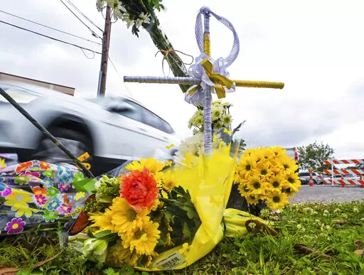 A collection of flowers and a cross with a halo are seen at the location where the body of Linda Frickey was recovered after she was carjacked and dragged to her death a day earlier on N. Pierce Street in New Orleans, Tuesday, March 22, 2022. New Orleans Police Department Superintendent Shaun Ferguson announced that four teenagers allegedly involved in the death of Frickey, 73, have been arrested. (Max Becherer/The Times-Picayune/The New Orleans Advocate via AP)