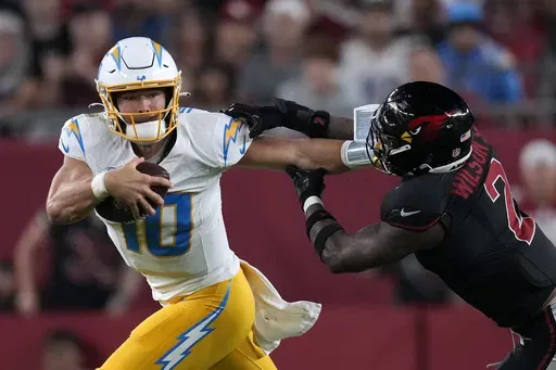 Los Angeles Chargers quarterback Justin Herbert (10) runs from Arizona Cardinals linebacker Mack Wilson Sr. (2) during the second half of an NFL football game, Monday, Oct. 21, 2024, in Glendale Ariz. (AP Photo/Matt York)