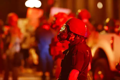 FILE -A Denver Police officer wears a gas mask before tear gas and rubber bullets were used to disperse protesters outside the State Capitol over the death of George Floyd, Thursday, May 28, 2020, in Denver. A federal jury’s $14 million award to Denver protesters injured during 2020 demonstrations over the killing of George Floyd could resonate nationwide as courts weigh more than two dozen similar lawsuits.(AP Photo/David Zalubowski, File)