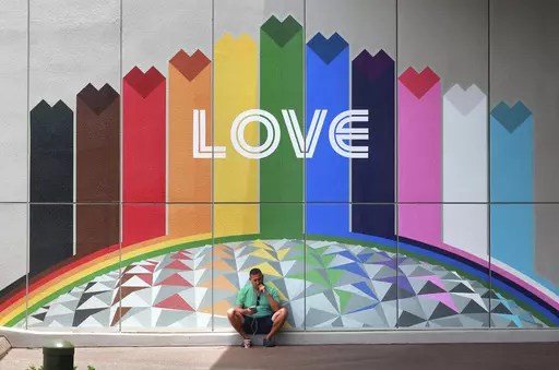 A guest finds a shady spot as a respite from the heat in front of a colorful mural adjacent to the Connections Cafe at Epcot at Walt Disney World, in Lake Buena Vista, Fla., Monday, July 10, 2023. The weather forecast calls for more of the same this week across Central Florida, with sticky humidity, highs in the low 90s and a chance of afternoon and evening thunderstorms. (Joe Burbank/Orlando Sentinel via AP)