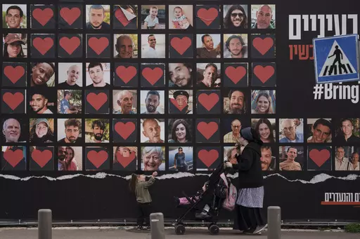 A woman and her children walk past a wall with photographs of hostages who were kidnapped during the Oct. 7 Hamas cross-border attack in Israel in Jerusalem, Israel, Monday, Feb. 26, 2024. (AP Photo/Leo Correa, File)