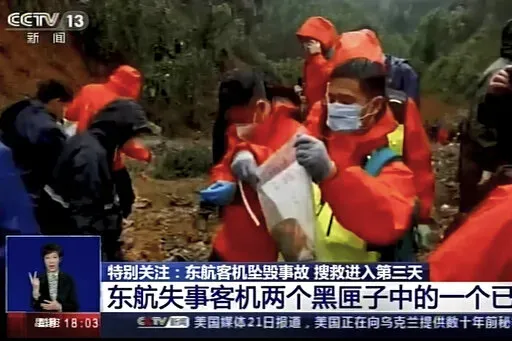 In this image taken from video footage run by China's CCTV, an emergency worker puts an orange-colored "black box" recorder into a plastic bag at the China Eastern flight crash site Wednesday, March 23, 2022, in Tengxian County in southern China's Guangxi Zhuang Autonomous Region. A Chinese aviation official said Wednesday that one of the two "black box" recorders had been found in severely damaged condition, two days after a China Eastern flight crashed in southern China with 132 people on boar