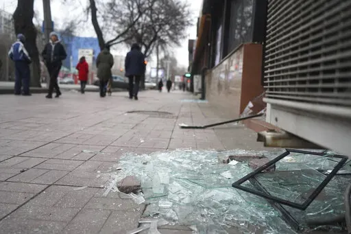 People walk past a shop with windows broken during clashes in Almaty, Kazakhstan, Monday, Jan. 10, 2022. Kazakhstan's health ministry says over 150 people have been killed in protests that have rocked the country over the past week. President Kassym-Jomart Tokayev's office said Sunday that order has stabilized in the country and that authorities have regained control of administrative buildings that were occupied by protesters, some of which were set on fire. (Vladimir Tretyakov/NUR.KZ via AP)