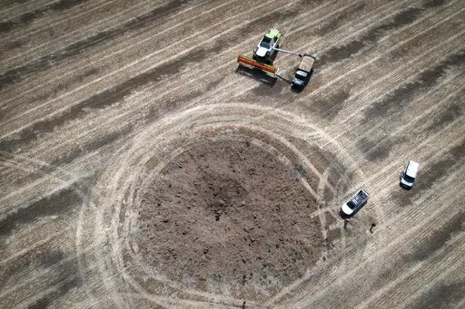A farmer collects harvest on a field ten kilometres from the front line where fierce battle is going, a crater left by the Russian rocket in the foreground, in the Dnipropetrovsk region, Ukraine, Monday, July 4, 2022. An estimated 22 million tons of grain are blocked in Ukraine, and pressure is growing as the new harvest begins. The country usually delivers about 30% of its grain to Europe, 30% to North Africa and 40% to Asia. But with the ongoing Russian naval blockade of Ukrainian Black Sea po