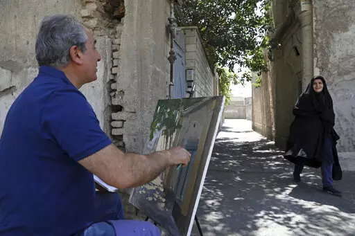 Painter Hassan Naderali greets a resident as he paints an old building in the historic neighborhood of Oudlajan, in Tehran, Iran, Monday, June 20, 2022. The overcrowded metropolis may be dusty and in need of beautification, but the old alleyways are nonetheless drawing throngs of artists out of their studios and into the streets. The practice thrived during the pandemic, as artists found solace and inspiration under the open sky when galleries and museums shuttered. (AP Photo/Vahid Salemi)