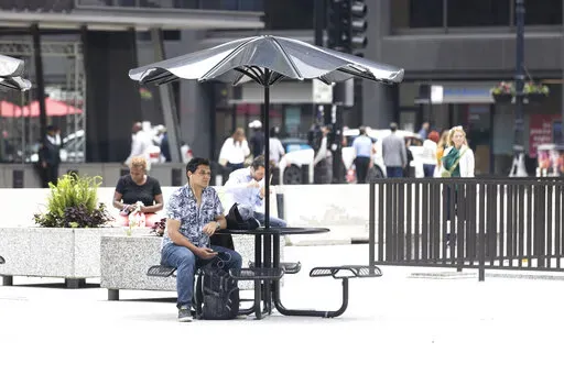 A person sits at a table at Daley Plaza in the loop, Monday, June 13, 2022, in Chicago. (Ashlee Rezin/Chicago Sun-Times via AP)