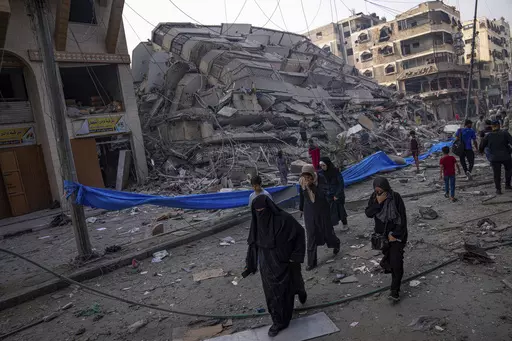 Palestinians walk by the rubble of a building after it was struck by an Israeli airstrike, in Gaza City, Sunday, Oct. 8, 2023. The militant Hamas rulers of the Gaza Strip carried out an unprecedented, multi-front attack on Israel at daybreak Saturday, firing thousands of rockets as dozens of Hamas fighters infiltrated the heavily fortified border in several locations by air, land, and sea, killing hundreds and taking captives. Palestinian health officials reported scores of deaths from Israeli a
