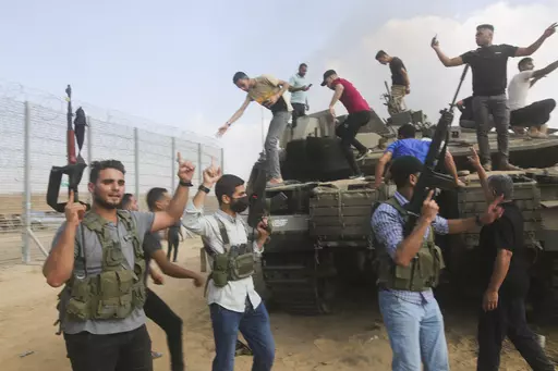 Palestinian militants, some with guns raised in the air, celebrate by an Israeli tank at the border fence of the Gaza Strip on Oct. 7, 2023. The militant Hamas rulers of the Gaza Strip carried out an unprecedented, multi-front attack on Israel at daybreak, firing thousands of rockets as dozens of Hamas fighters infiltrated the heavily fortified border in several locations by air, land, and sea and catching the country off-guard on a major holiday. (AP Photo)