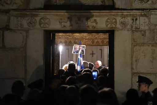 A man holds a picture of the former king of Greece Constantine with his wife, as others wait to enter in the Chapel of Saint Eleftherios as the coffin of the former king of Greece Constantine lies in repose in Athens, Monday, Jan. 16, 2023. Constantine died in a hospital late Tuesday at the age of 82 as Greece's monarchy was definitively abolished in a referendum in December 1974. (AP Photo/Petros Giannakouris)