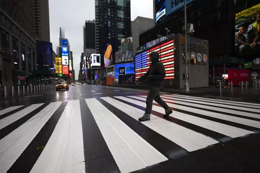 A man crosses the street in a nearly empty Times Square, which is usually very crowded on a weekday morning in New York on March 23, 2020. (AP Photo/Mark Lennihan, File)