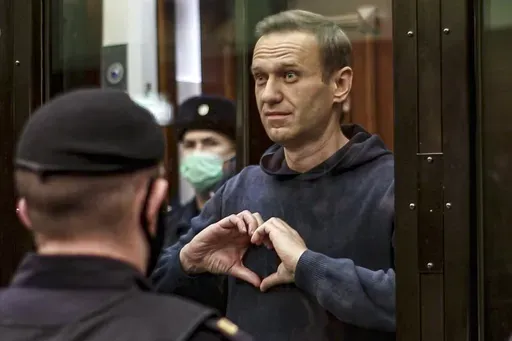In this image made from a video provided by Moscow City Court, Russian opposition leader Alexei Navalny makes a heart symbol while standing in the defendants’ cage during a hearing into his 2014 criminal conviction in Moscow, Russia, on Feb. 2, 2021. (Moscow City Court via AP, File)