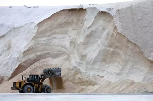 A front-end loader works in front of a pile of road salt, Friday, Jan. 28, 2022, in Chelsea, Mass. Residents and officials in the Northeast and mid-Atlantic regions of the U.S. are bracing for a powerful winter storm expected to produce blizzard conditions Friday and Saturday. (AP Photo/Michael Dwyer)