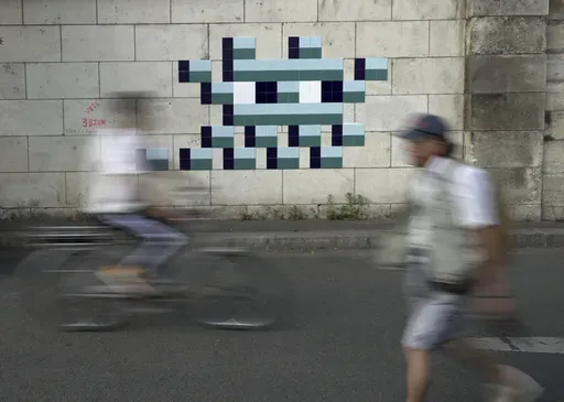 A cyclist rides in front of an Olympic-themed new mosaic by the mysterious French street artist known only by the name Invader, Wednesday Aug. 7, 2024, on the banks of the Seine River, during the 2004 Summer Olympics, in Paris, France. (AP Photo/John Leicester)