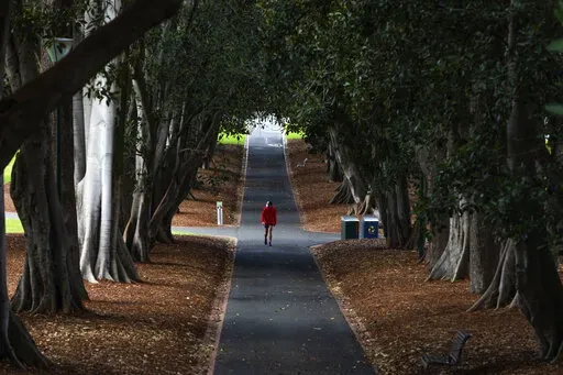 A man wearing a mask is seen walking in a Melbourne park as Melbourne goes into Stage 4 Lockdown due to the spread of COVID-19, Wednesday, Aug. 5, 2020. The coronavirus variant has swept across Australia despite its high vaccination rate and strict border policies that kept the country largely sealed off from the world for almost two years. (AP Photo/Asanka Brendon Ratnayake, File)