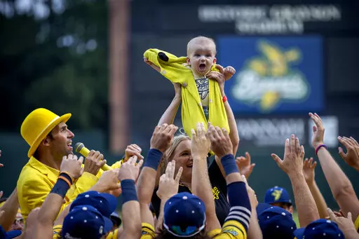 Molly Knutson holds her baby James Knutson high above the players as the Savannah Bananas present the Banana Baby to the crowd while playing the theme song from the movie "Lion King" over the public address system, Saturday, June 11, 2022, in Savannah, Ga. (AP Photo/Stephen B. Morton)