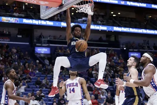 New Orleans Pelicans forward Keion Brooks Jr., top, hangs from the rim after dunking against Philadelphia 76ers guard Ricky Council IV (14) during the first half of an NBA basketball game in New Orleans, Monday, March 24, 2025. (AP Photo/Matthew Hinton)