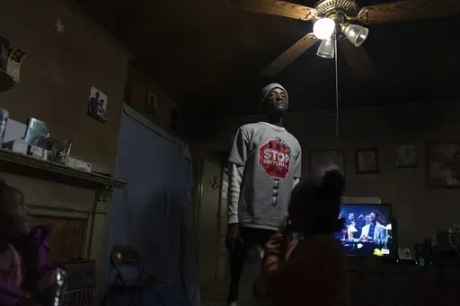 Tyrone Heard stands in his living room with his kids Karinina, 8, Tyrone, Jr., 7, and Kylee, 5, after they arrived home from school, Friday, Dec. 6, 2024, in Alexander City, Ala. Heard's uncle, Willie Craytwon was killed while on work release riding in an Alexander City Work Center transport van that crashed in April. (AP Photo/Carolyn Kaster)