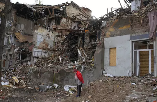 Local resident Nina, 72, stands near her house, ruined by the Russian shelling a month ago in central Slavyansk, Donetsk region, Ukraine, Saturday, Oct. 29, 2022. She keeps living in this house and collects wooden debris to make an outdoor fire for cooking. (AP Photo/Efrem Lukatsky)